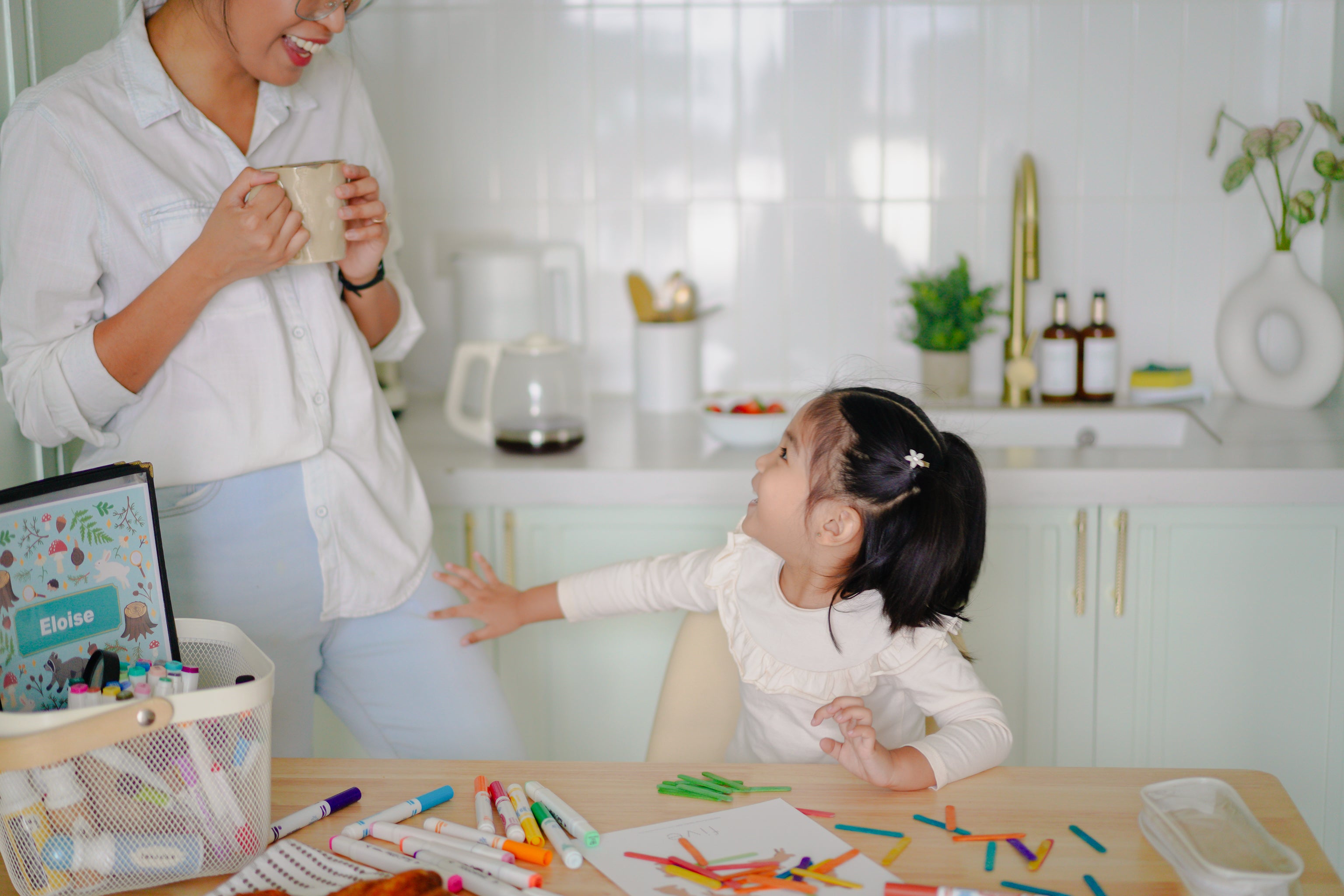 Woman and child in a kitchen with art supplies on a table