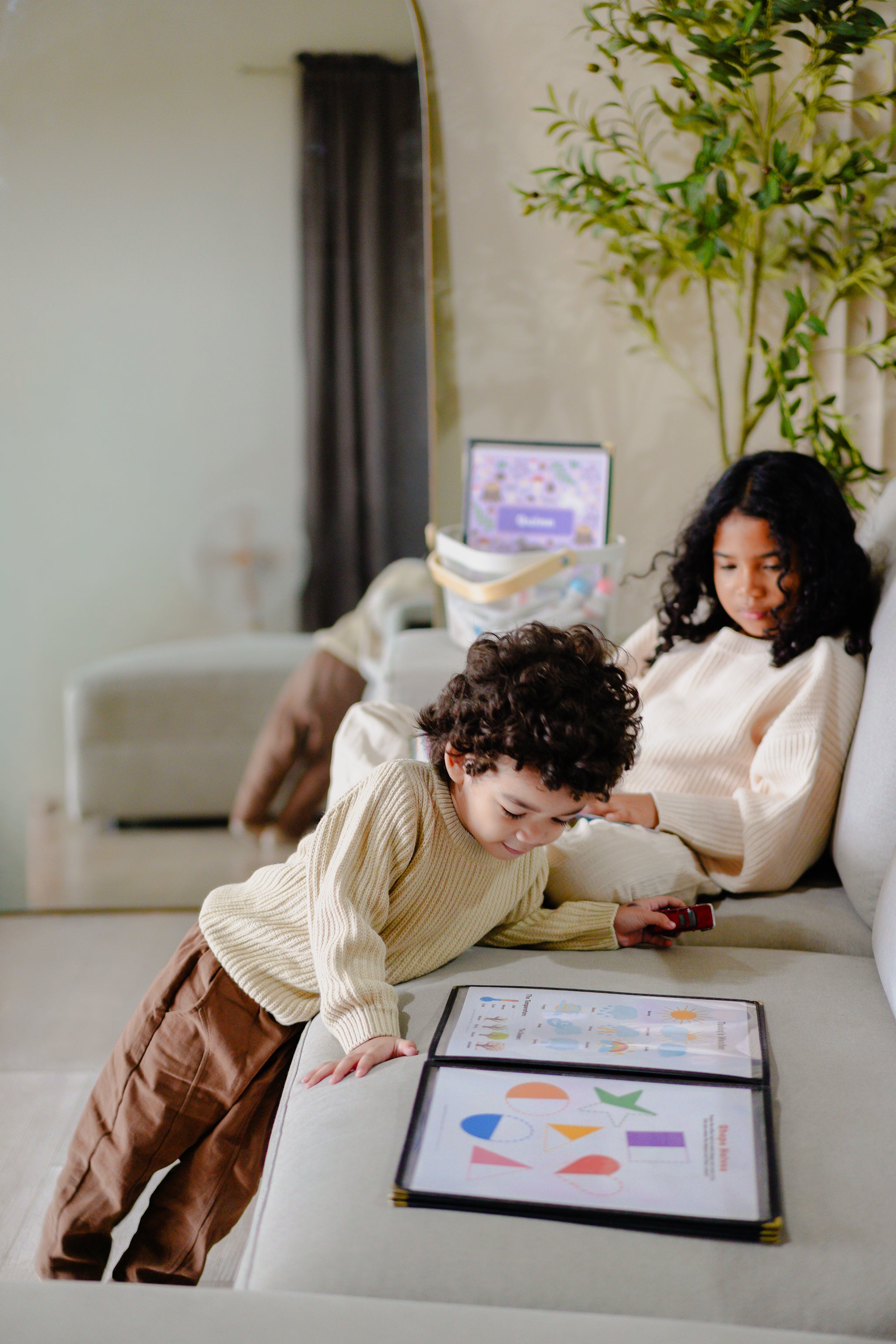 Two children sitting on a couch with educational materials and a tablet.
