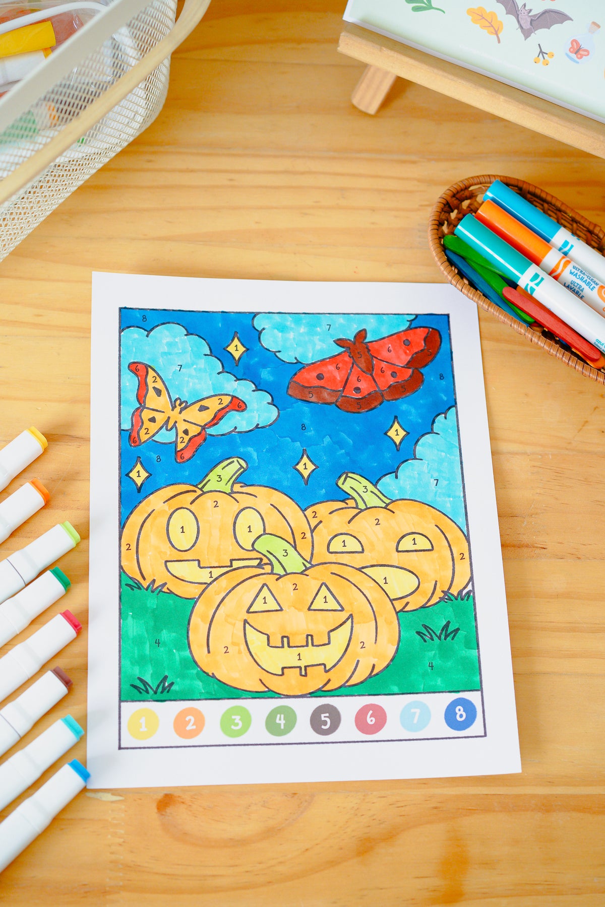 children's color by number page of jack-o-lantern pumpkins on a table with markers