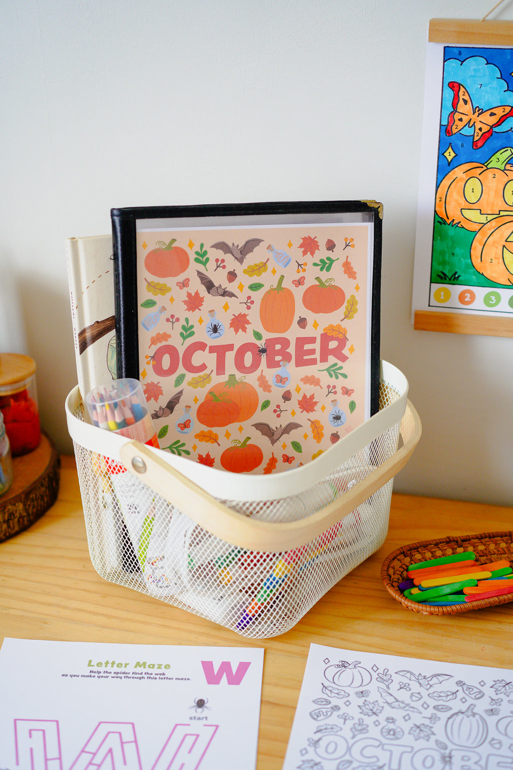 October activity pages for kids on a table with craft supplies, in a white basket with a wooden handle.