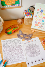 children's printable activity pages featuring bats, spiders and pumpkins laid out on a table with markers and craft supplies.