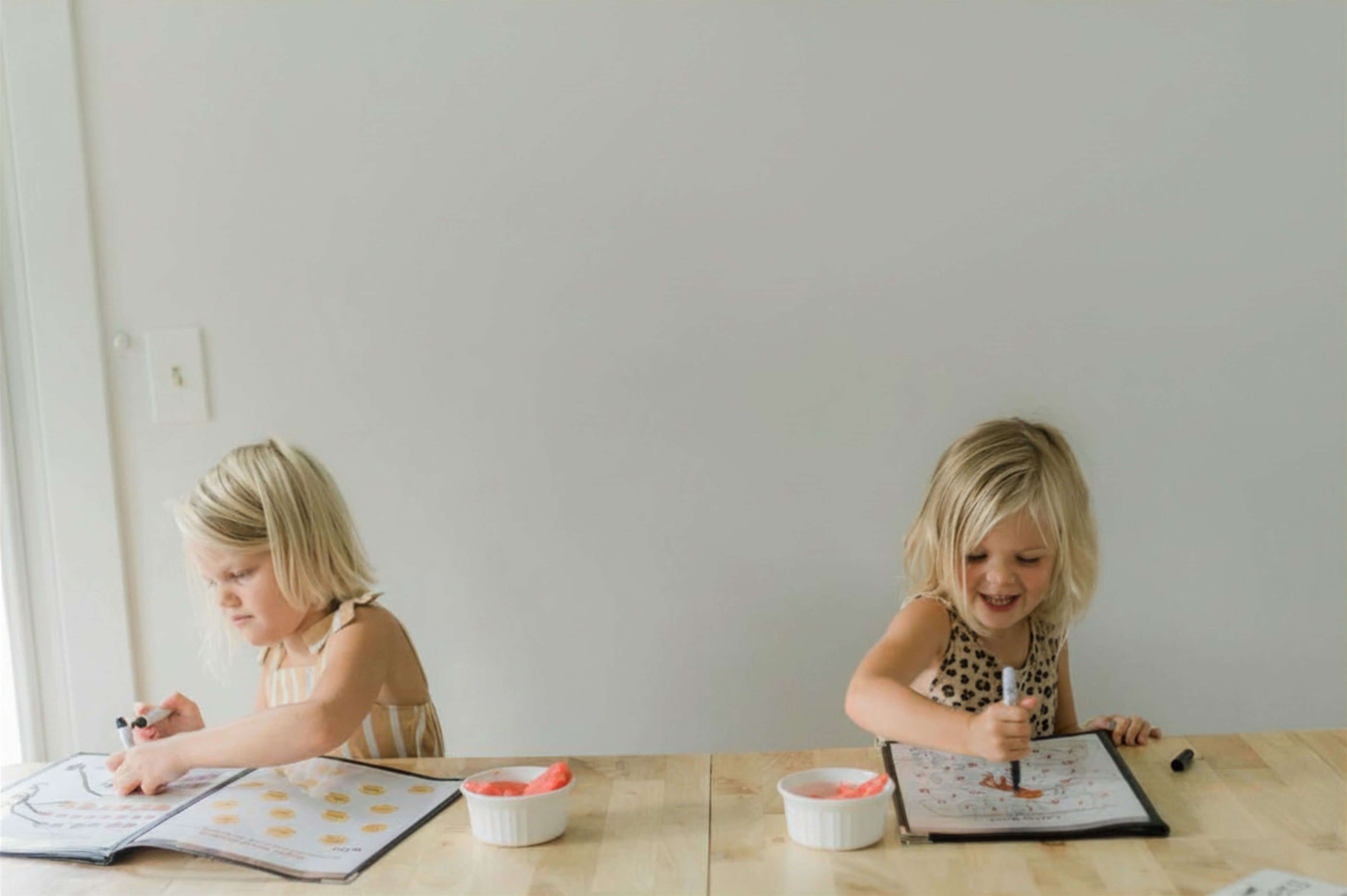 Two children sitting at a table with coloring books and crayons.