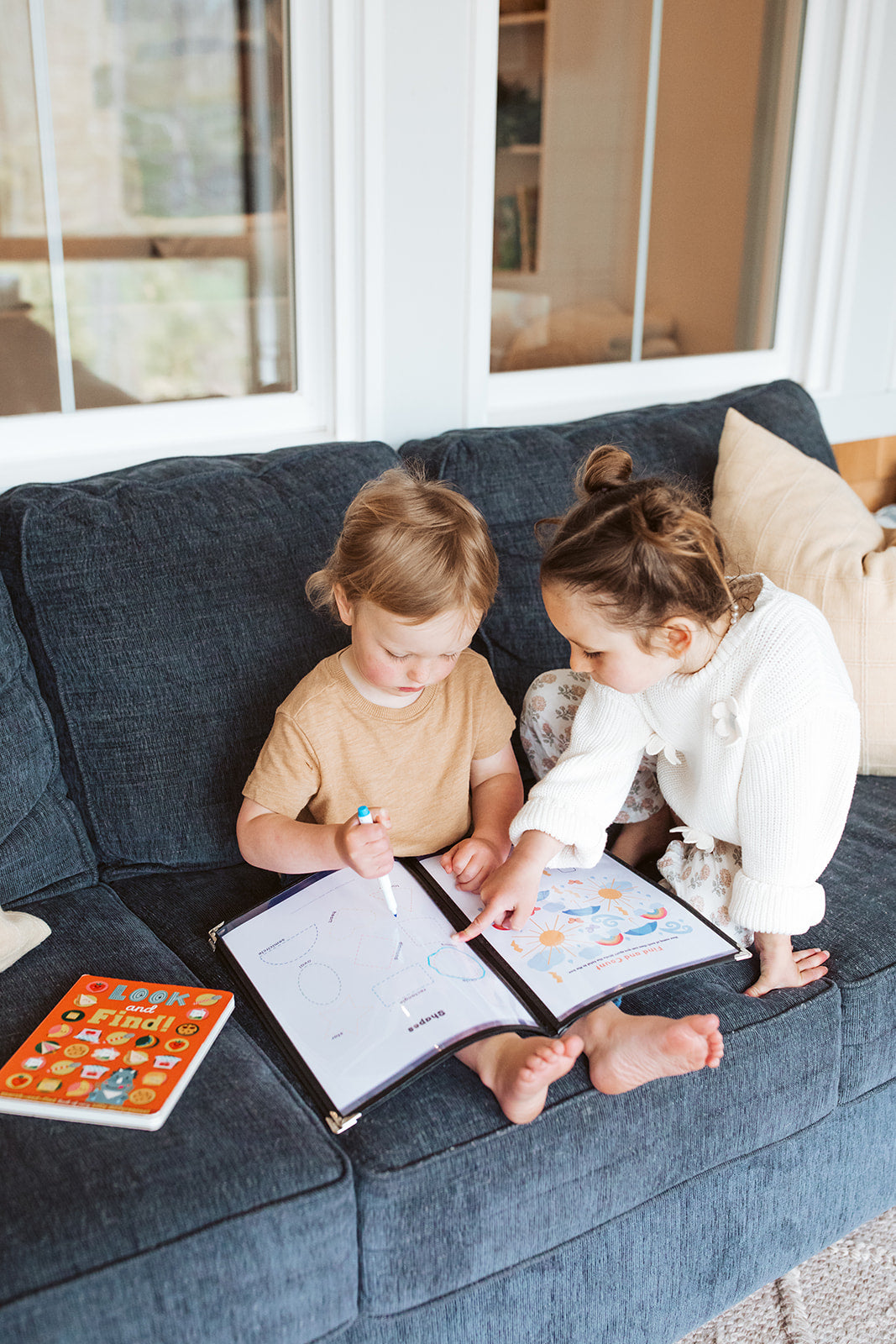 Two children sitting on a blue couch, looking at a book together.