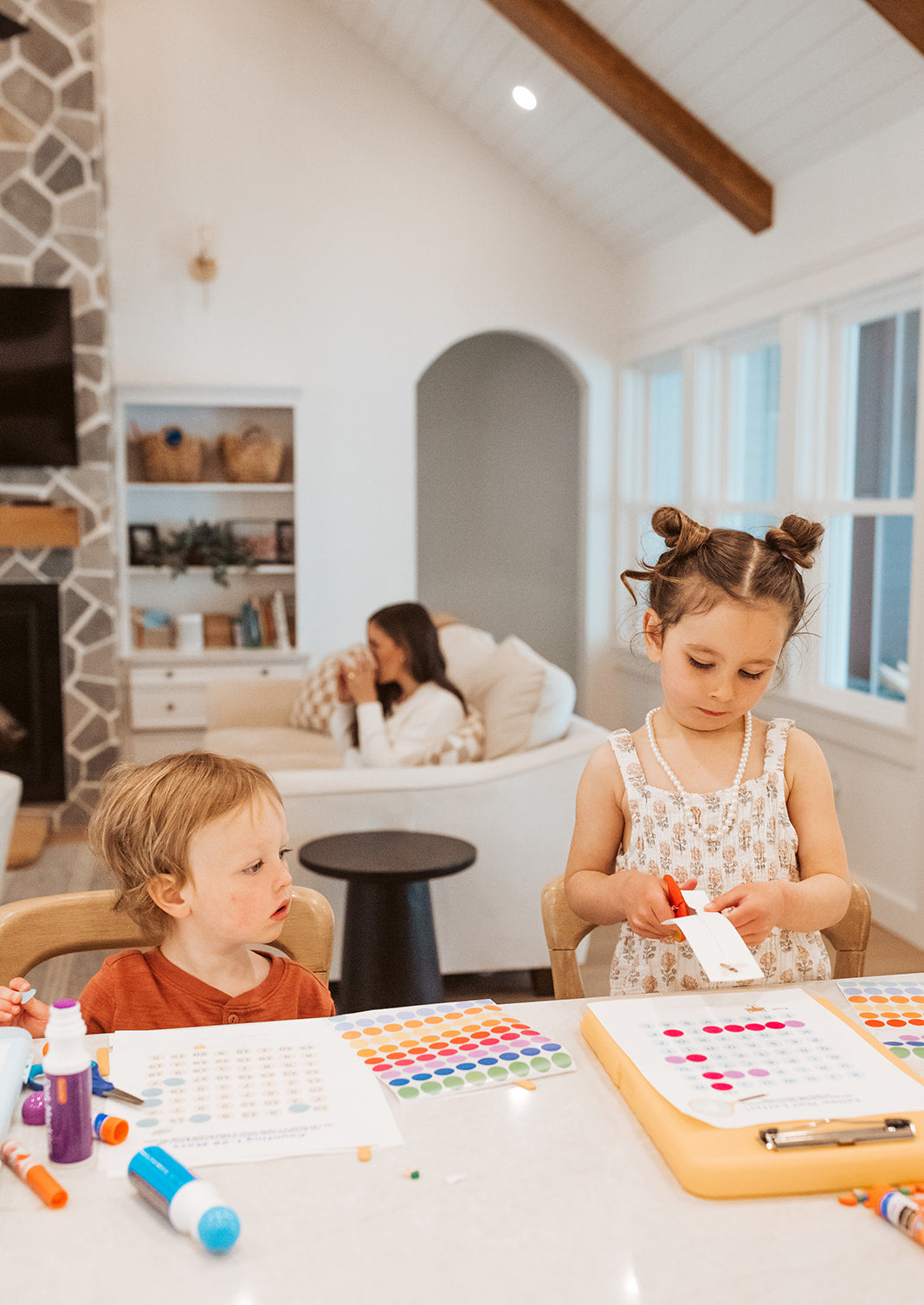 Two children sitting at a table with art supplies in a cozy living room.